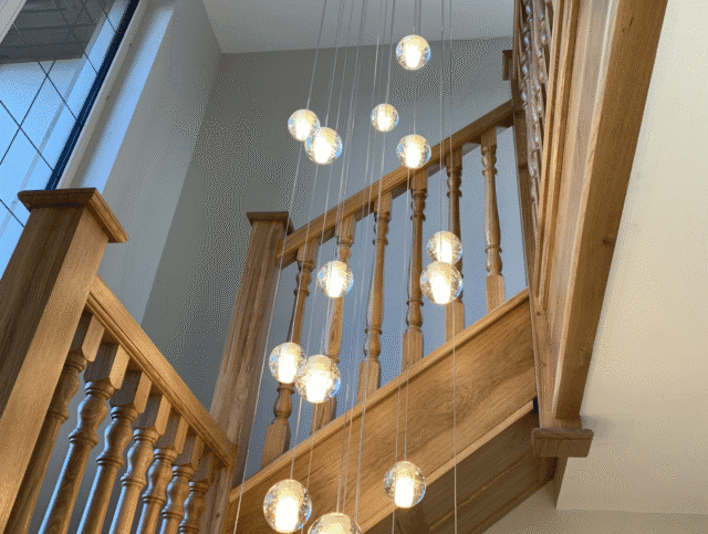 Multiple multi-level hanging lights in the center of a wooden staircase